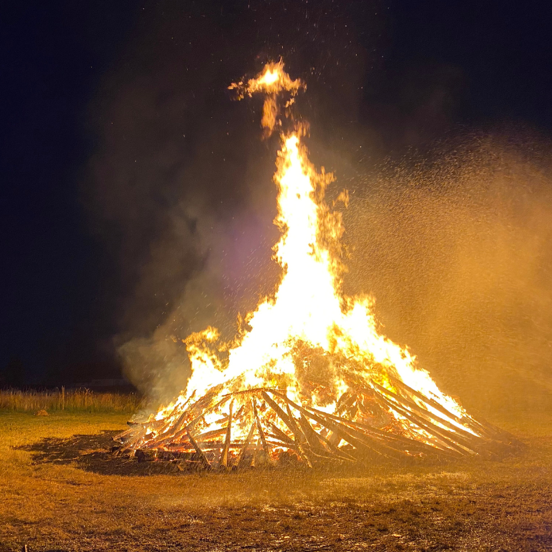 Gro&szlig;es Johannisfeuer auf einem Feld, das hell in der Nacht lodert